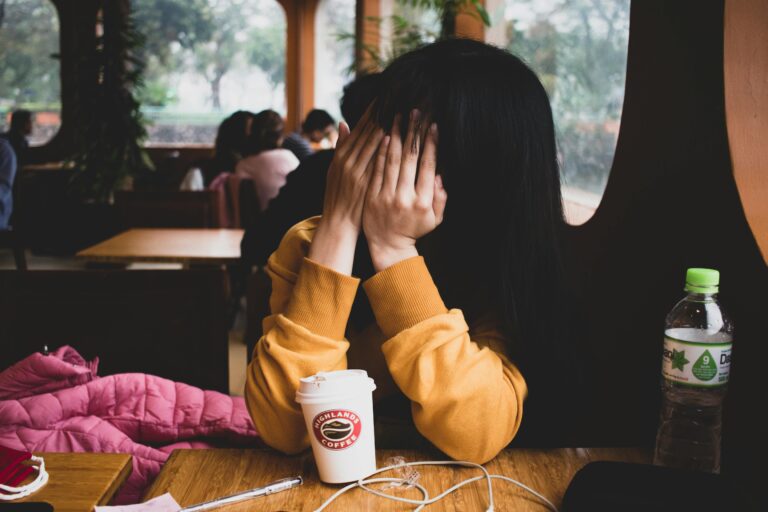 Woman with dark hair Covering Her Face while sitting in a diner